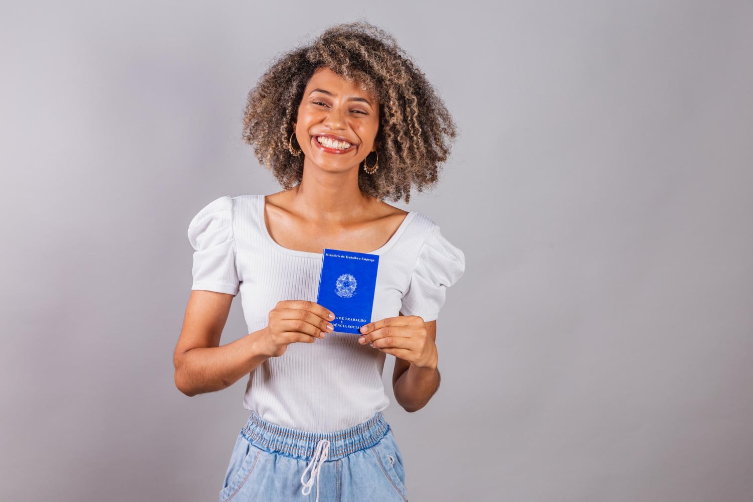 Mulher sorridente segurando carteira de identidade azul, representando documentação de trabalho, relacionada ao o que é a CTPS.